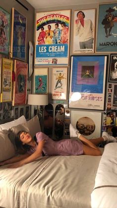 a woman laying on top of a bed in a room filled with posters and pictures