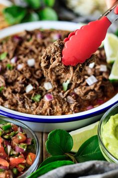 a person scooping some food out of a bowl with guacamole and lime wedges