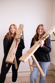 two women standing next to each other holding wooden objects