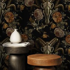 a vase sitting on top of a wooden stool next to a wallpapered wall