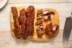 bacon strips on a wooden cutting board next to a knife and plate with food in it