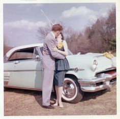 a man and woman standing next to an old car