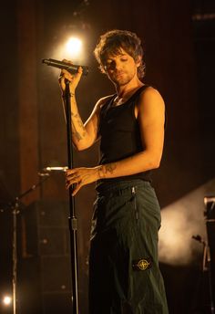 a man with tattoos on his arm holding a microphone in front of a stage light