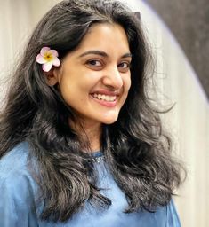 a woman with long dark hair and a flower in her hair smiles at the camera