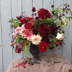 a vase filled with lots of flowers sitting on top of a table next to a wooden fence