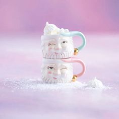 two ceramic mugs with faces on them sitting in the snow, one has a ring around its neck