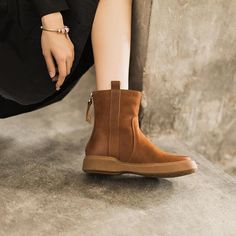 a close up of a person's legs wearing brown boots and sitting on the ground