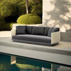 a couch sitting on top of a cement slab next to a swimming pool with trees in the background