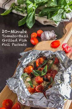 the foil is covered with tomatoes and other vegetables on a cutting board next to some basil leaves