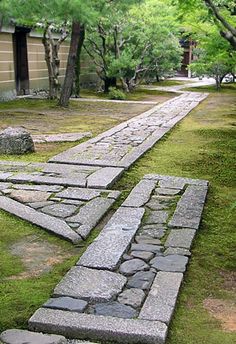 a stone path in the middle of a grassy area with trees and bushes around it