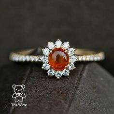 a close up of a ring with an orange stone in the center and white diamonds around it