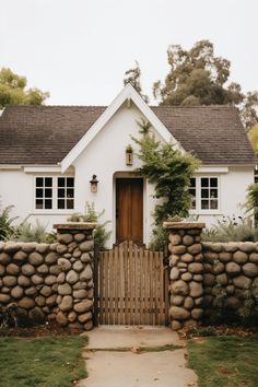 a white house with a wooden gate and stone wall around the front entrance to it