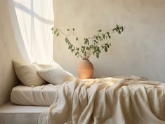 a bed with white sheets and a plant in a vase on the end of it