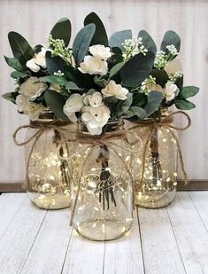 three mason jars with white flowers and greenery in them