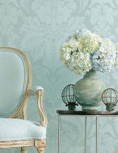 a chair and vase with flowers in it on a table next to a wallpaper