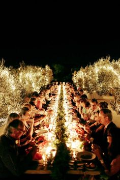 a group of people sitting at a long table with food and candles in front of them