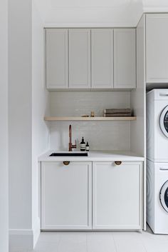 a washer and dryer in a white laundry room with cabinets on either side