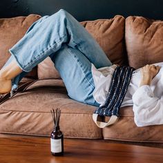 a woman laying on top of a brown couch next to a bottle of wine and an air freshener