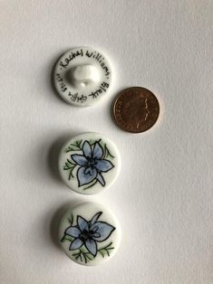 three buttons with blue flowers on them next to a quarter penny for the price of one