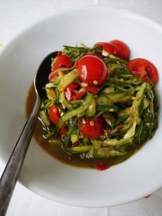 a white bowl filled with green vegetables and sauce on top of a table next to a fork