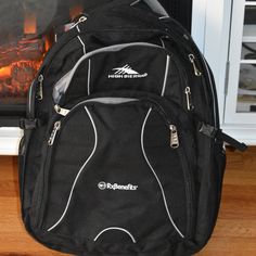 a black backpack sitting on top of a wooden floor in front of a fire place