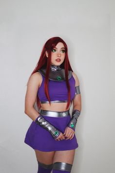 a woman with red hair wearing a purple outfit and silver gloves is standing in front of a white wall