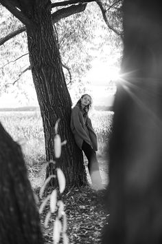 black and white photograph of a woman sitting on the ground next to a large tree