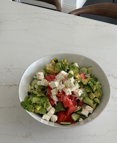 a white bowl filled with cucumber, tomato and feta cheese on top of a table