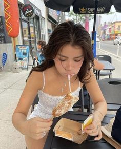 a woman sitting at a table eating food with an umbrella over her head on the street