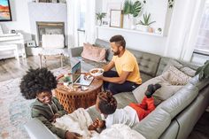 three people sitting on a couch in front of a table with laptops and food