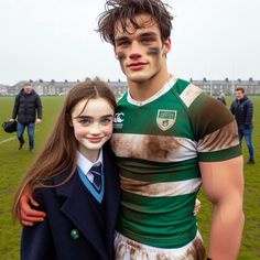 a young man and woman standing next to each other on a field with people in the background