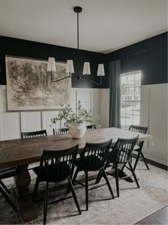 a dining room table with black chairs and a painting on the wall in the background