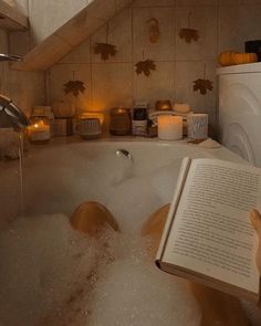 an open book sitting in a bathtub filled with water next to candles and pumpkins