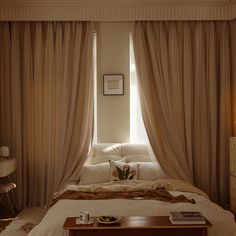 a bed sitting under a window next to a table with a lamp on top of it