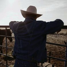 a man wearing a cowboy hat standing next to a fence with horses in the background