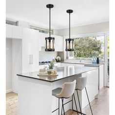 a kitchen island with three stools and two pendant lights hanging from it's ceiling