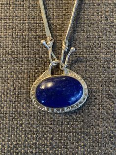 "Beautiful AAA quality Lapis stone that I cut and polished with my lapidary equipment.  The oval stone stone has a beautiful deep blue color  and measures 1.5\" wide, 1\" tall and .25\" deep. I have set the stone horizontally in a sterling silver bezel setting.  The handmade sterling silver bar chain is 18\" in length with 3 bar on each side with  front hook closures that attach to the pendant. Each bar is 1.75 \" in length with a 14k gold fill wire connecting each bar and is finished off around the back of the neck with 3mm round rolo chain for comfort. I am happy to accommodate adjustments for the length of the chain." Unique Blue Necklace With Polished Finish, Handmade Oval Lapis Lazuli Necklace, Oval Sapphire Cabochon Necklace, Oval Sapphire Necklace With Cabochon Cut, Blue Oval Pendant Necklace With Polished Finish, Sapphire Sterling Silver Oval Pendant Necklace, Blue Oval Link Necklaces For Gift, Blue Oval Link Necklace For Gift, Artisan Blue Necklace Stamped 925