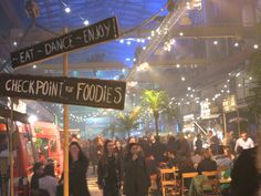 a group of people are walking through an indoor food court with street signs in the foreground