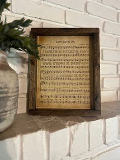 a wooden frame with sheet music on it next to a potted plant and brick wall