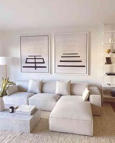 a living room filled with white furniture and art on the wall above it's fireplace