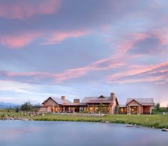 a large house sitting on top of a lush green field next to a lake under a cloudy sky