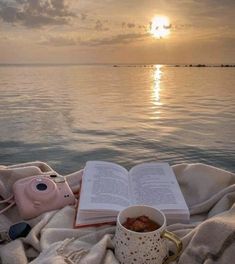 an open book sitting on top of a blanket next to a cup