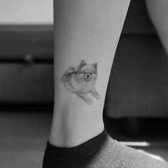 a small pomeranian dog tattoo on the right ankle and leg area is shown in black and white