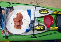 a green kayak filled with food on top of the beach next to other items