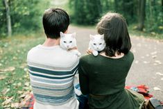 a man and woman are sitting on a blanket with their white cat in their lap