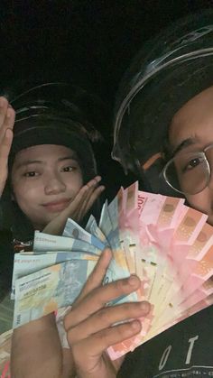 two people holding up money in front of their face and smiling at the camera with both hands