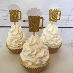 three cupcakes with white frosting and gold decorations