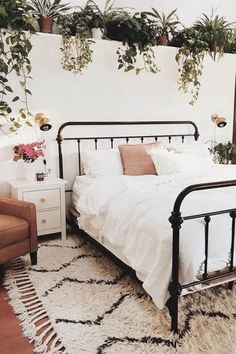 a bed with white sheets and pillows in a bedroom next to a brown chair, potted plant on the wall