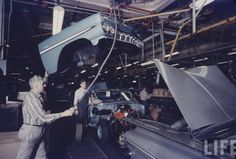 two men working on an assembly line in a car factory, one is holding the hood up