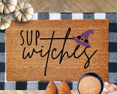 a welcome mat with the words sup witches on it next to two pumpkins